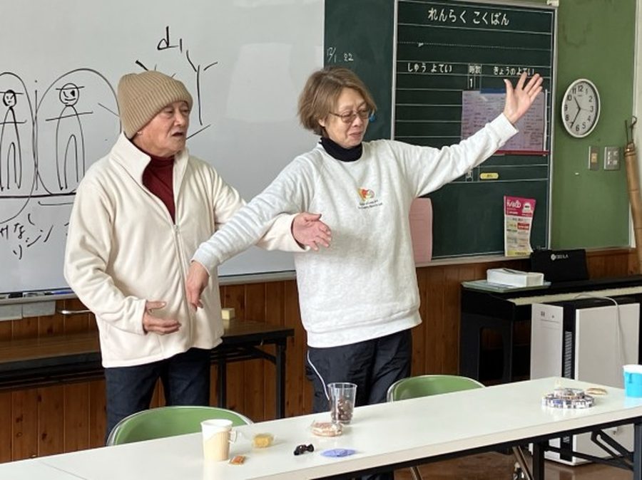 公民館で身振りを交えて住民に語りかける講師2人の様子